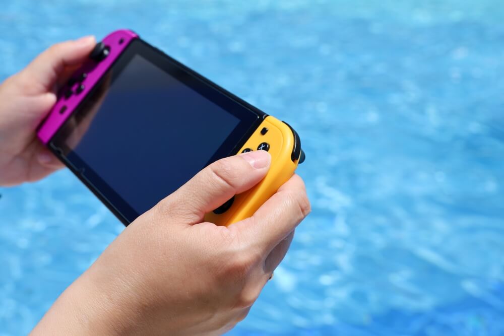 Woman,Playing,Game,On,Handheld,Console,Near,The,Swimming,Pool,